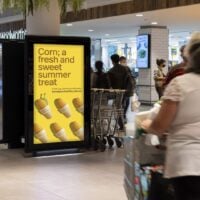 A bright advertising sign outside a supermarket reads, Corn, a fresh and sweet summer treat