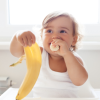 A young child in a high chair eating a banana